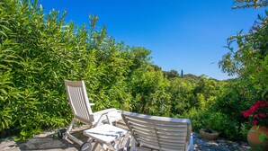 A garden with a white chair and table, surrounded by greenery and a clear blue sky. - Holiday Home 'Maison De Gathen' with Sea View, Shared Pool and Air Conditioning (Cavalaire-sur-Mer)