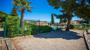 A fenced outdoor area with a pool, palm trees, and a building in the background. - Holiday Home 'Maison De Gathen' with Sea View, Shared Pool and Air Conditioning (Cavalaire-sur-Mer)