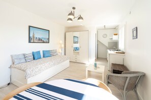 A modern bedroom with a bed, bedside tables, a chair, a painting, and a kitchenette. - Cozy Studio in Soorts-Hossegor – Close to the Lake and Beach for a Relaxing Stay (Soorts-Hossegor)