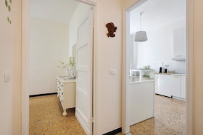 Un pasillo que conduce a una cocina con armarios blancos, un colgante de techo y una puerta decorada con un detalle ornamental.
