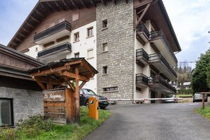 Un immeuble à plusieurs étages, doté de balcons, d’une enseigne en bois et d’une voiture garée devant.