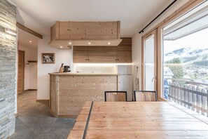 Une cuisine moderne avec des meubles en bois, un coin repas doté d’une grande table et une vue sur un paysage montagneux par le biais d’une grande fenêtre.