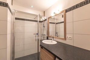 Une salle de bain moderne avec une douche à l’italienne en verre, un lavabo blanc et un grand miroir.