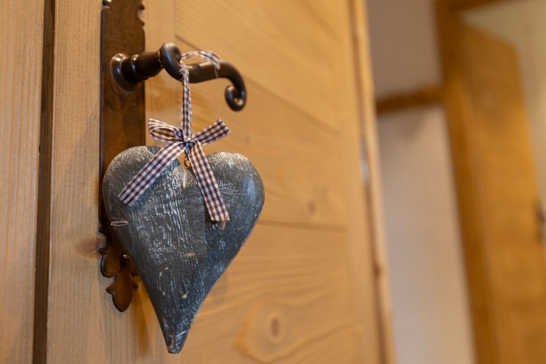 A heart-shaped decoration with a checkered ribbon hanging on a wooden door handle.