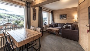 Un interior de madera con una mesa de comedor, sofá y vista a un pueblo.
