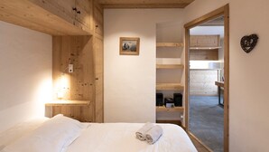 Un dormitorio con techo de madera, una cama con ropa de cama blanca, una mesita de noche con lámpara, un cuadro enmarcado en la pared y vista a la habitación contigua.
