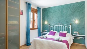 A bedroom with a bed, curtains, a window, and a teal accent wall. - 'Denia Sur' Apartment with Mountain Views, Wi-Fi, and Air Conditioning (La Xara)