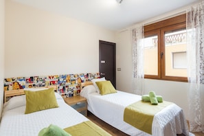 A hotel room with two beds, a wooden headboard with comic strip wallpaper, a window with lace curtains, and a door with a sign.