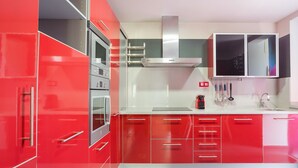 A modern kitchen with red cabinets, stainless steel appliances, and a white countertop. - 'Denia Sur' Apartment with Mountain Views, Wi-Fi, and Air Conditioning (La Xara)