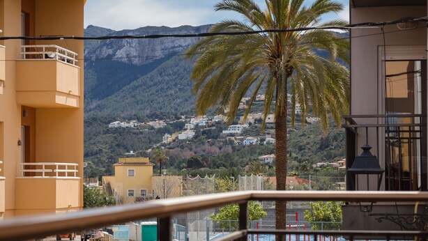 A balcony with a view of a mountain, a palm tree, and buildings in the background. - 'Denia Sur' Apartment with Mountain Views, Wi-Fi, and Air Conditioning (La Xara)