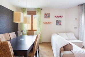 A room with a dining table, chairs, a bed, and a window with curtains.