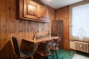 A wooden-paneled room with a wooden table, chairs, a radiator, and a window with a decorative view.