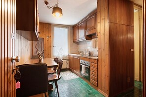 A kitchen with wooden cabinets, a dining table, chairs, a hanging light fixture, and a radiator.