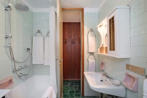 A bathroom with a shower, sink, and wooden door.