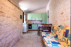 A compact kitchen with green cabinets, a dining table, and a sofa with a colorful blanket.