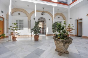 A spacious indoor area with a high ceiling, white walls, and a tiled floor. There are several potted plants and a large stone planter.