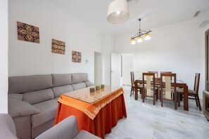 A living room with a sofa, a dining table with chairs, and a chandelier.