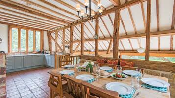 A rustic dining area with wooden beams, a large table set for four, and a view of the outdoors through large windows.