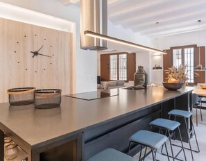 Een moderne keuken met een groot schiereiland, barstoelen, een klok en een hangende lamp.