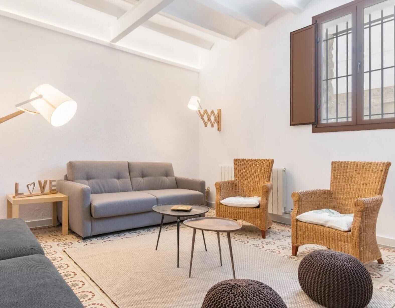 A cozy living room with a sofa, two wicker chairs, a small table, and a lamp.