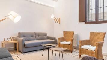 A cozy living room with a sofa, two wicker chairs, a small table, and a lamp.