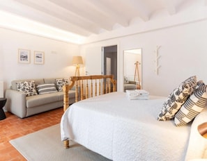 A bedroom with a bed, a wooden headboard, a sofa, a lamp, a mirror, and a rug.