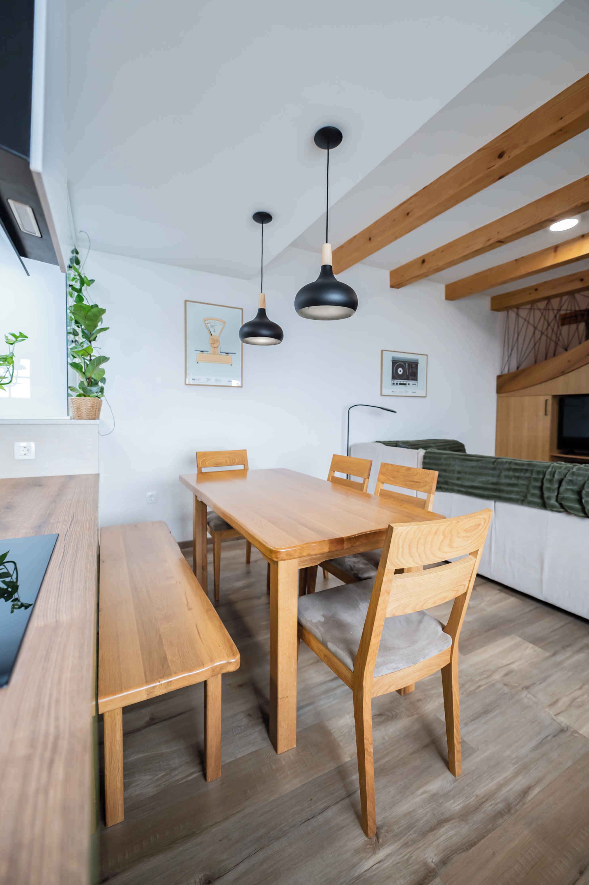 A modern kitchen with wooden beams, a dining table with chairs, and pendant lighting.