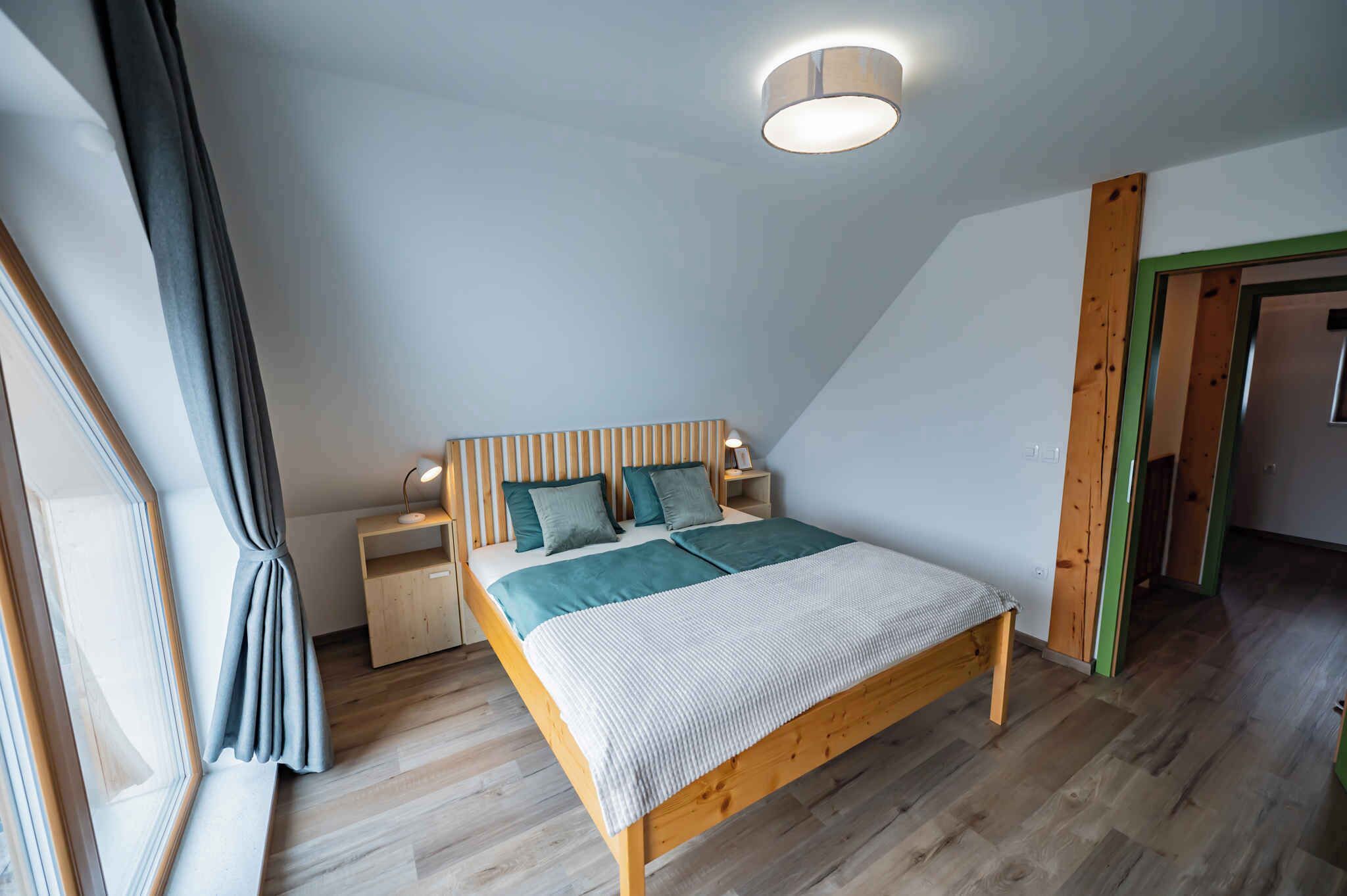 Een slaapkamer met een houten bed, een nachtkastje, een bedlamp en een raam met gordijnen.