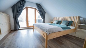 A bedroom with a wooden bed, a nightstand, a lamp, and a view of a building through a large window.