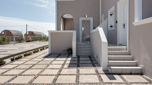 A building with a staircase leading to a door, a small garden area with potted plants, and a clear sky. - St George Sea View Double Room – Private Jacuzzi with Sea View (Santorini)