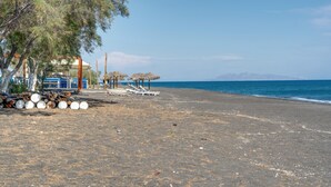 A beach with umbrellas, lounge chairs, and a building with blue walls. - St George Sea View Double Room – Private Jacuzzi with Sea View (Santorini)