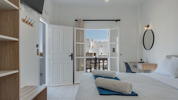 Een hotelkamer met een bed, een bureau, een stoel, een televisie en een balkon.
