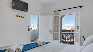 Hotelkamer met een bed, een televisie, een balkon met tafel en stoelen en een deur naar buiten.