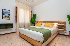 A bedroom with a wooden bed, white bedding, a green throw, yellow patterned pillows, a plant, and a wall-mounted shelf. - Apartment 'Home Centrum 2' with Sea View, Wi-Fi and Air Conditioning (Giarre)