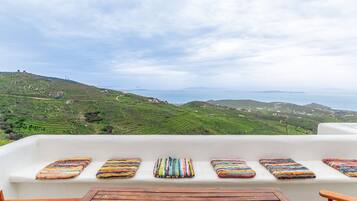 Un espacio de estar al aire libre con asientos blancos y cojines de colores, con vistas a un paisaje verde con campos escalonados y colinas lejanas.