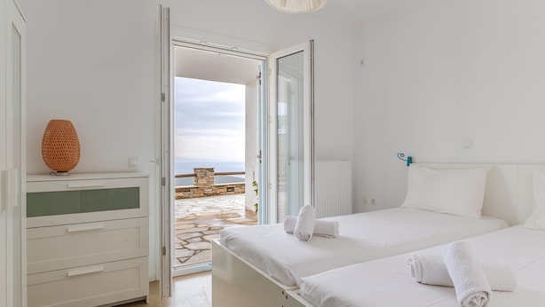 A bedroom with a bed, a dresser, and a view of the sea through an open door. - Holiday Home 'Modern New Tinos' with Sea View, Private Terrace and Wi-Fi (Tinos)