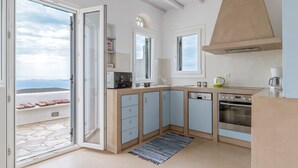 A kitchen with a stone floor, a built-in oven, and a view through an open door. - Holiday Home 'Modern New Tinos' with Sea View, Private Terrace and Wi-Fi (Tinos)