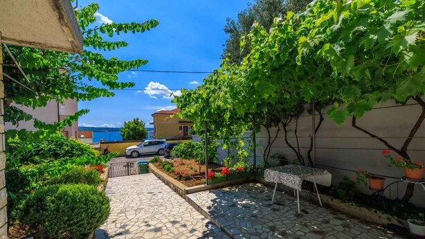 A paved courtyard with stone tiles, a small table, potted plants, and a car parked in the background. - Holiday apartment with air conditioning and terrace (Dramalj)