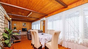 A cozy dining area with a wooden ceiling, a dining table with chairs, and a large window with lace curtains. - Holiday apartment with air conditioning and terrace (Dramalj)