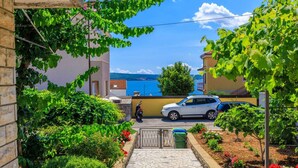 A residential street with a paved pathway leading to a gate, surrounded by lush greenery and flowering plants. - Holiday apartment with air conditioning and terrace (Dramalj)