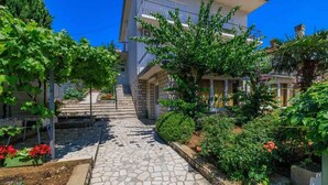 A courtyard with a stone pathway, surrounded by lush greenery and flowering plants. - Holiday apartment with air conditioning and terrace (Dramalj)