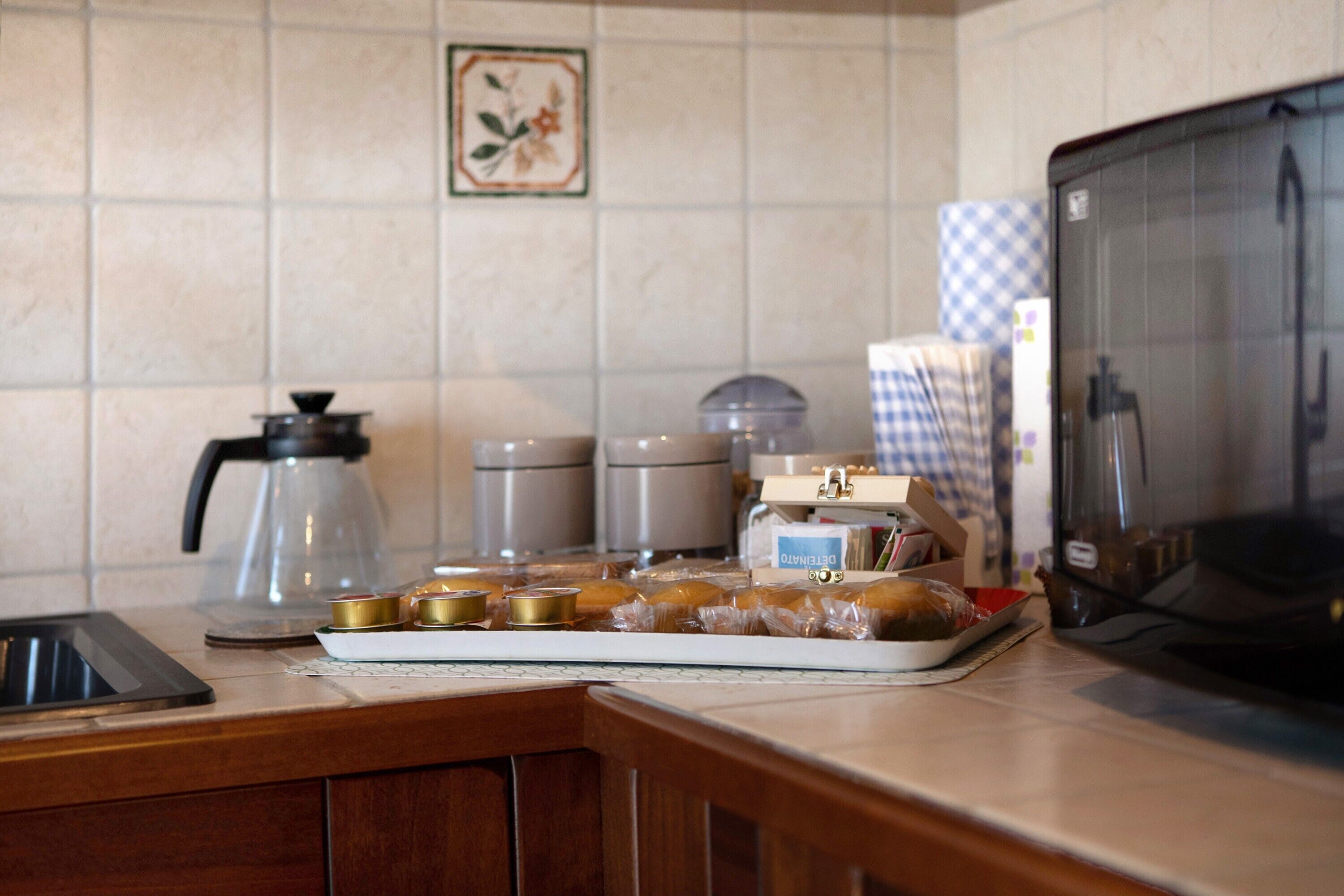 A kitchen counter with a coffee maker, a kettle, a microwave, and a tray of pastries.