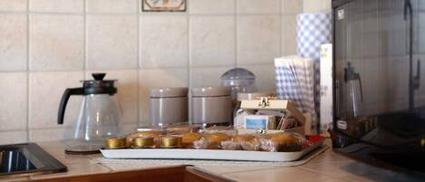 A kitchen counter with a coffee maker, a kettle, a microwave, and a tray of pastries.