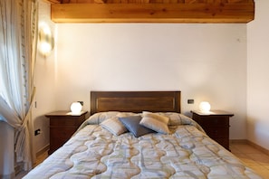 A bedroom with a wooden headboard, a bed with patterned bedding, two bedside lamps, and a curtain on the window.