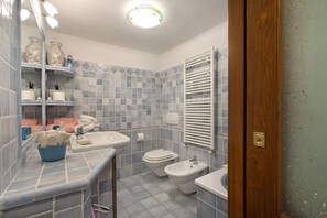 A bathroom with a sink, toilet, bidet, and a mirror with lights.
