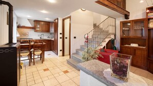 A kitchen with wooden cabinets, a dining table with chairs, a staircase, and a red sofa. - Apartment 'Manu - Blavy Nus' with Mountain View, Private Terrace and Wi-Fi (Blavy)