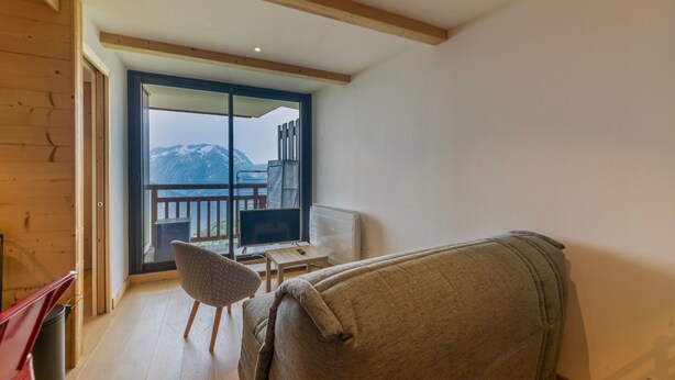 A room with a balcony, a chair, a table, and a sofa. - Apartment 'Alpe D'huez' with Mountain View and Balcony (Huez)