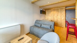A room with a sofa, a chair, a small table, a red stool, and a wooden door. - Apartment 'Alpe D'huez' with Mountain View and Balcony (Huez)