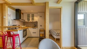 A compact kitchen with wooden beams, a dining area with red chairs, a patterned armchair, and a bed in the adjacent room. - Apartment 'Alpe D'huez' with Mountain View and Balcony (Huez)