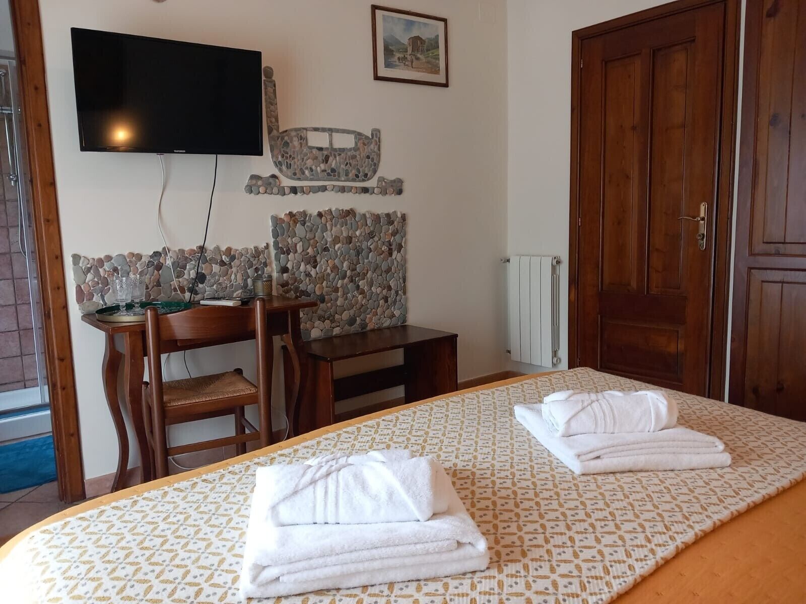 A hotel room with a bed, a desk, a chair, a television, a stone wall, and a wooden door.